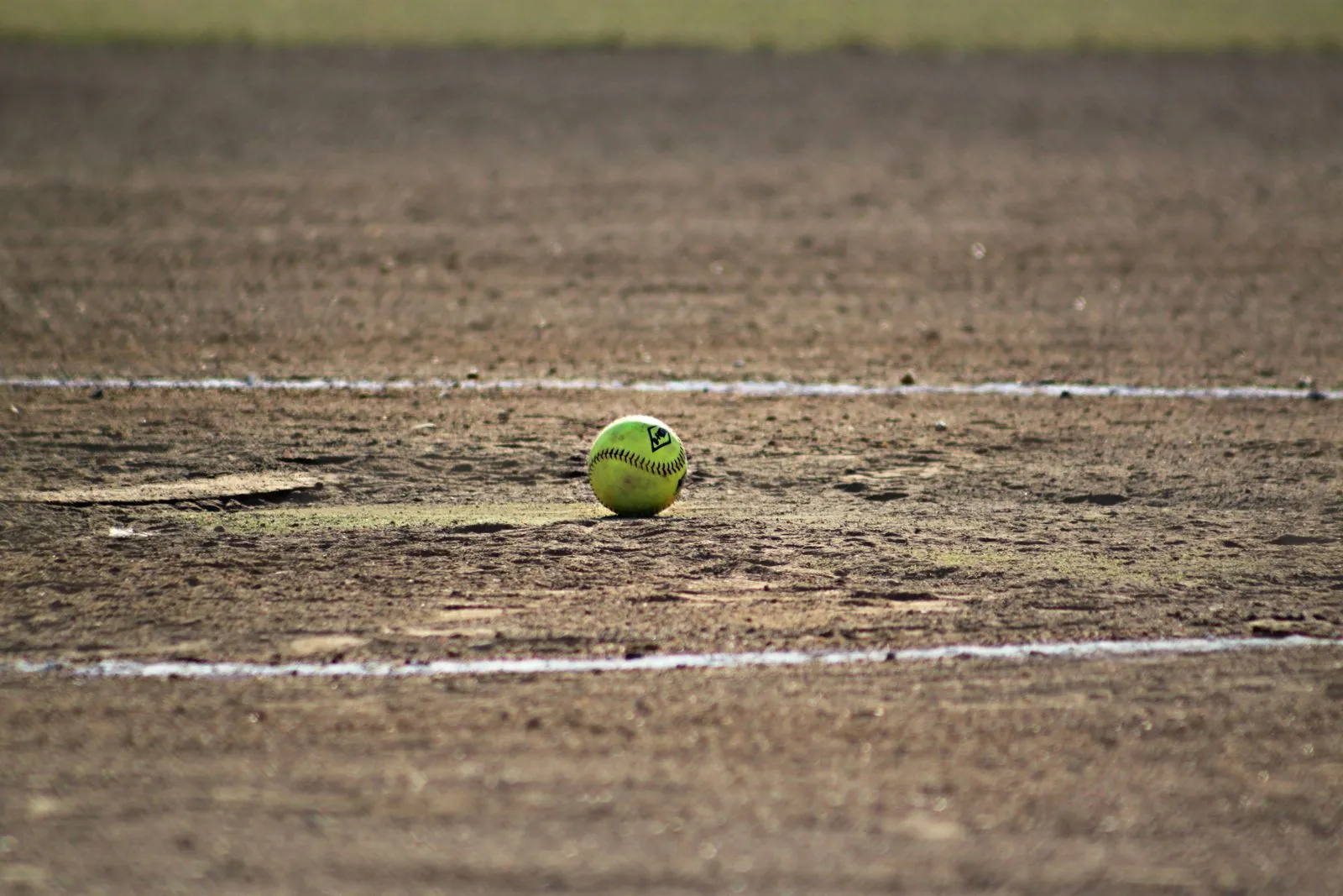 A lone softball sits on a dusty field, capturing the essence of the sport.
